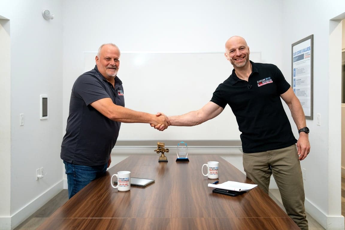 Two restoration company leaders shaking hands across a conference table