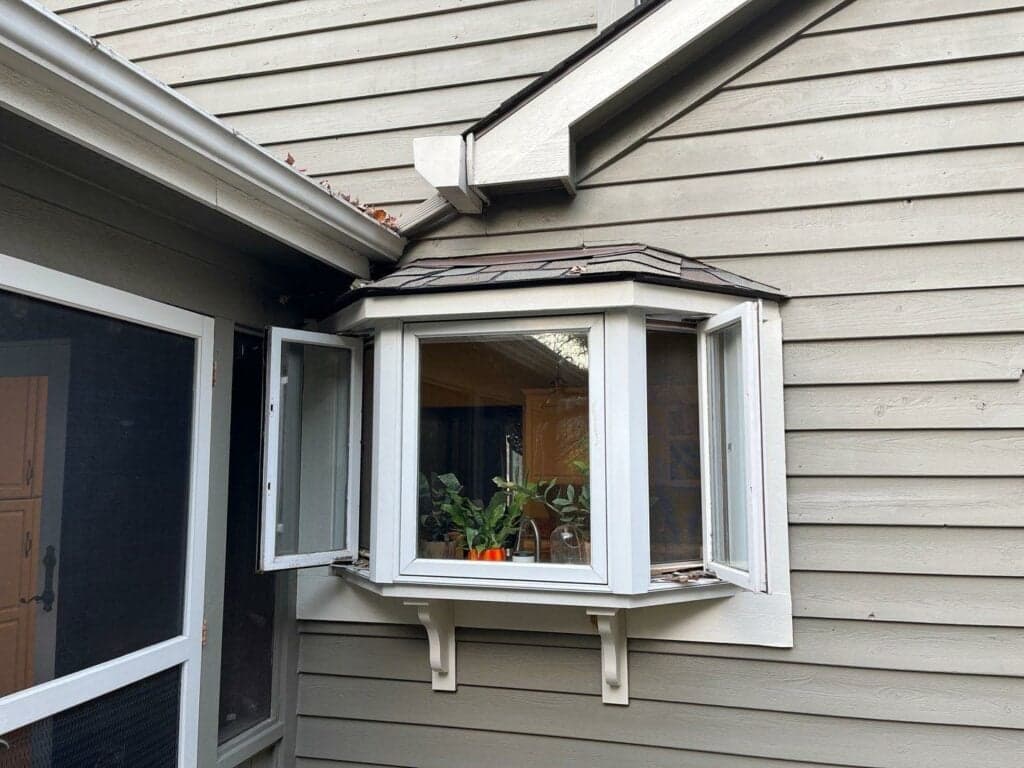 An open, white trimmed window with plants on its sill.