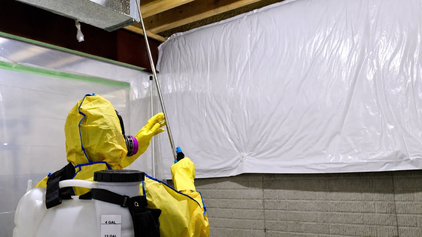 A Mold and Air Duct Pros technician treating framing in full protective equipment inside containment
