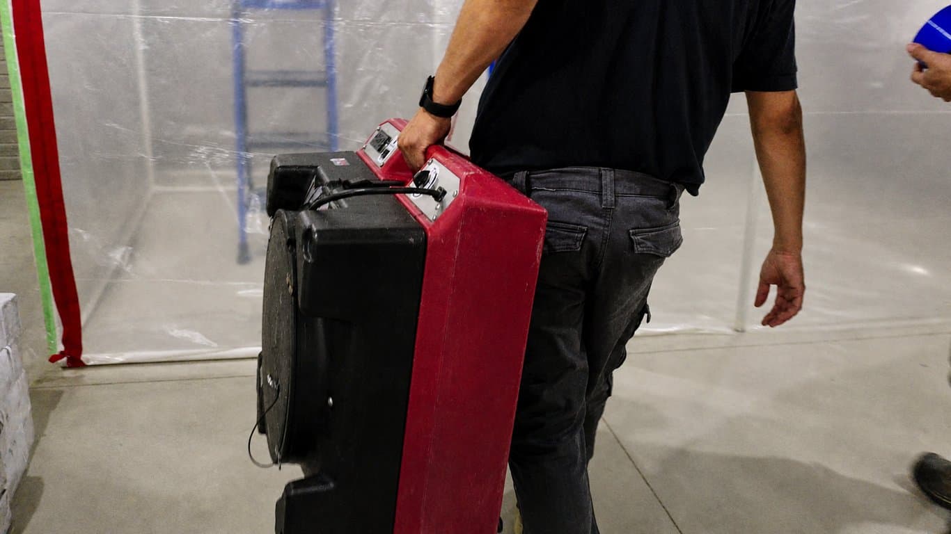 A technician moving HEPA air-control equipment into a contained remediation area