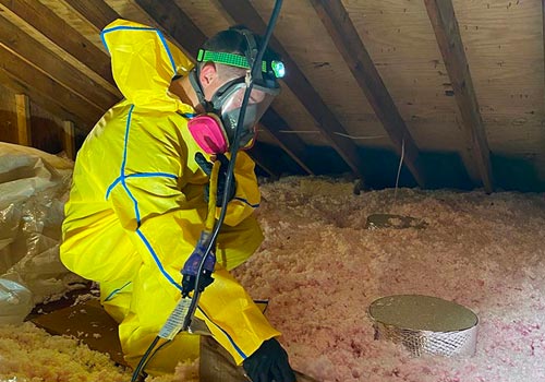 A team member from Mold and Air Duct Pros works in attic wearing respirator 