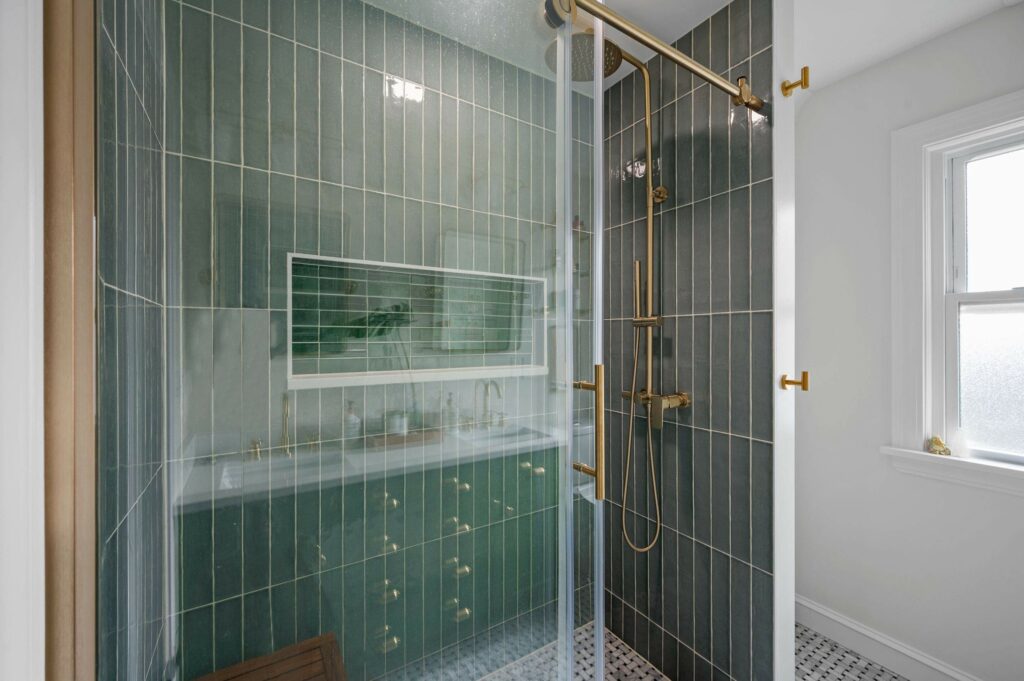 A large walk-in shower with green tile backsplash and sliding glass door
