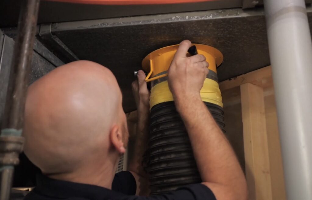 Mold and Air Duct Pros team member cleaning the air ducts. Connecting large vacuum system to capture dust particles and debris.
