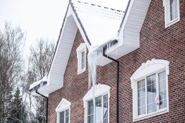 A suburban brick home with ice and snow on the roof. 
