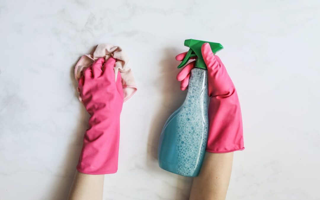A pair of hands wearing bright pink gloves hold a blue spray bottle