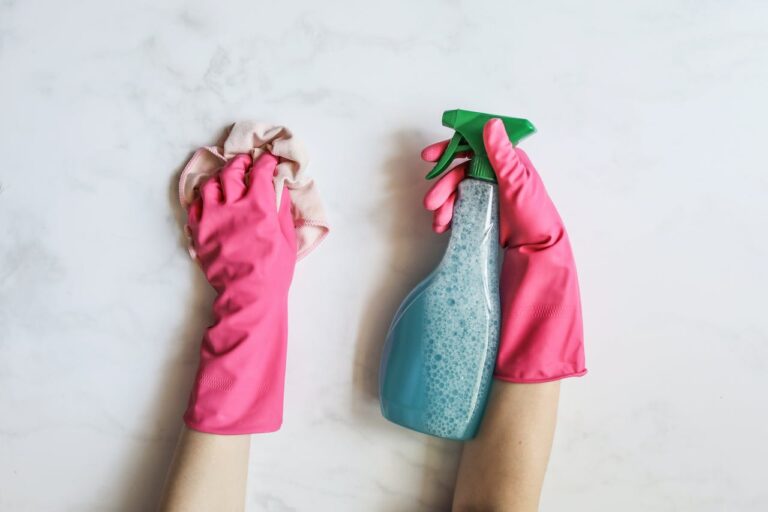 A pair of hands wearing bright pink gloves hold a blue spray bottle