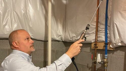 A containment zone is created in a basements using plastic sheeting. A team member from Mold and Air Duct Pros works on mold cleanup.
